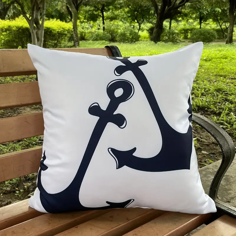 Contemporary white outdoor pillow cover featuring a large, stylized navy blue anchor graphic positioned at an angle, displayed on an outdoor wooden bench for nautical décor - 18x18.