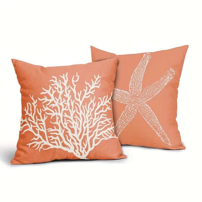 Two coral-colored linen pillow covers featuring a white coral branch design and a white starfish motif, displayed together on a textured fabric background.