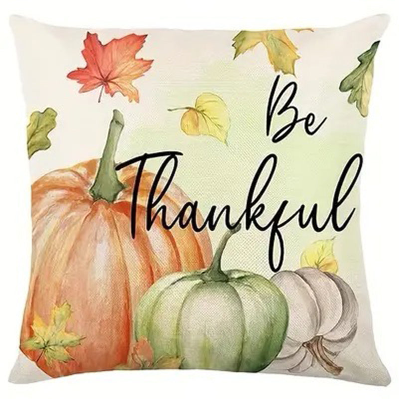 Pillow cover with Be Thankful script and pumpkins in orange and green with scattered autumn leaves.
