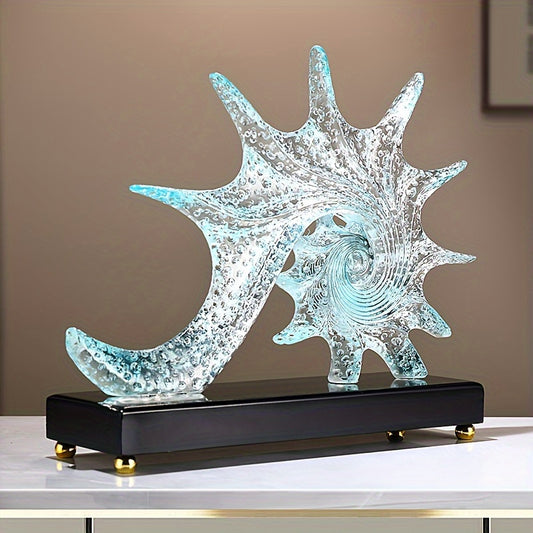 A modern blue-tinted resin spiral shell sculpture set on a sleek black pedestal with gold feet. - Coastal Pillows Plus