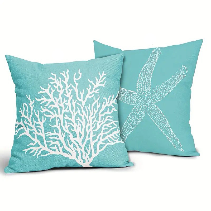 Two cerulean blue linen pillow covers featuring a white coral branch design and a white starfish motif, displayed together on textured fabric.