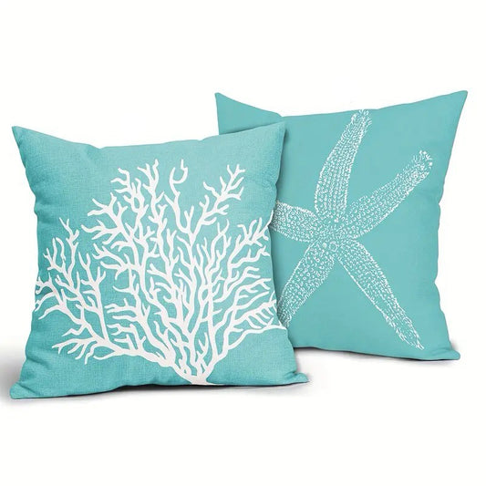 Two cerulean blue linen pillow covers featuring a white coral branch design and a white starfish motif, displayed together on textured fabric.