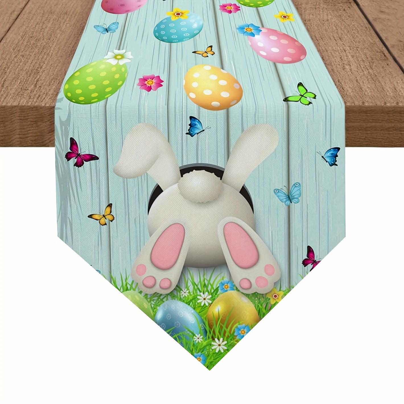 Fetching 13x90 inch triangular Easter table runner featuring a bunny bottom diving into a hole, with eggs and butterflies on a blue wood-grain background, styled on a table for spring holiday décor – Coastal Pillows Plus