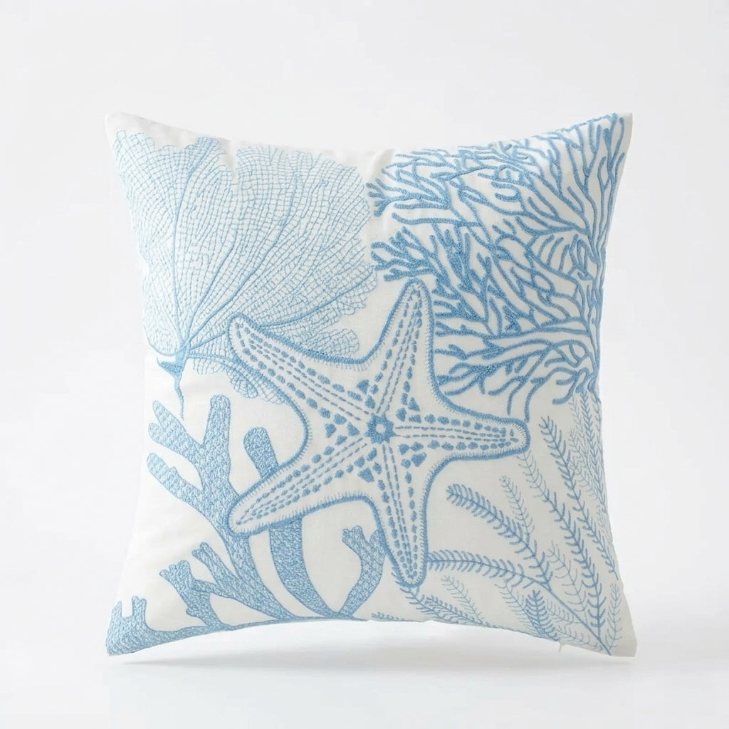 Blue and white coastal pillow cover with embroidered starfish, coral, and shell reef design on light fabric for coastal home decor.