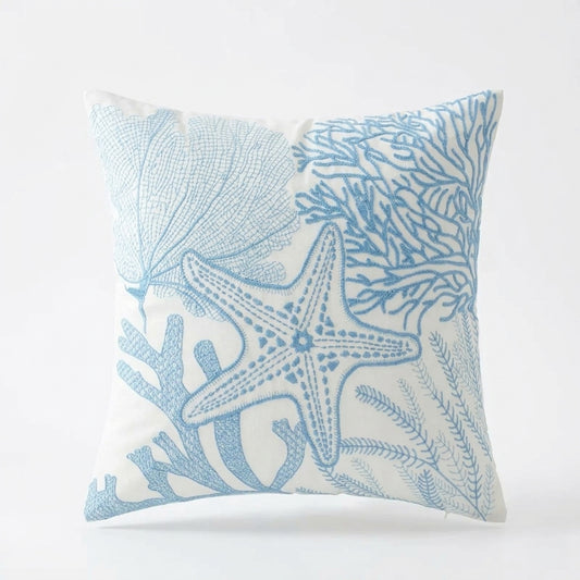 Blue and white coastal pillow cover with embroidered starfish, coral, and shell reef design on light fabric for coastal home decor.