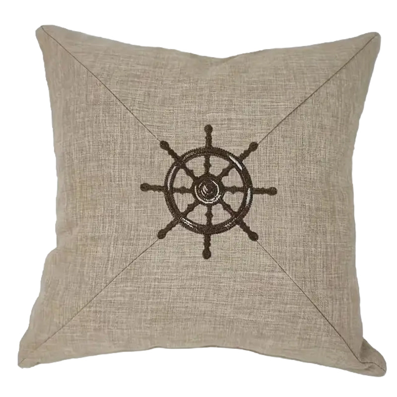 Neutral pillow cover with embroidered ship wheel design centered on textured fabric for coastal and nautical home decor.