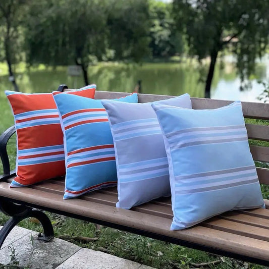 Set of four outdoor waterproof pillow covers with horizontal stripe designs in red and blue tones displayed on an outdoor bench.
