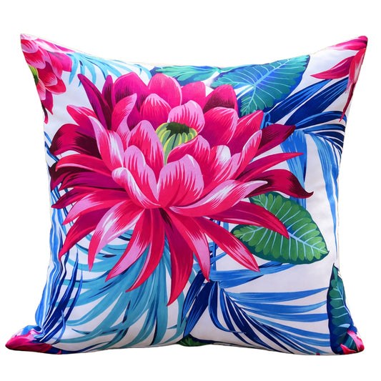 Outdoor 18x18 pillow cover featuring a large pink tropical flower with blue and green leaves on a white background, displayed on a wooden park bench near a lake. Waterproof cover, insert not included.